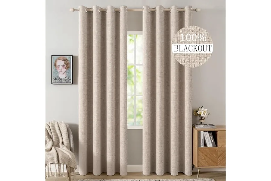 Cream linen blackout curtains hung high on a black rod in a bright neutral bedroom with soft folds, white blinds, wood accents, and cozy minimalist styling.