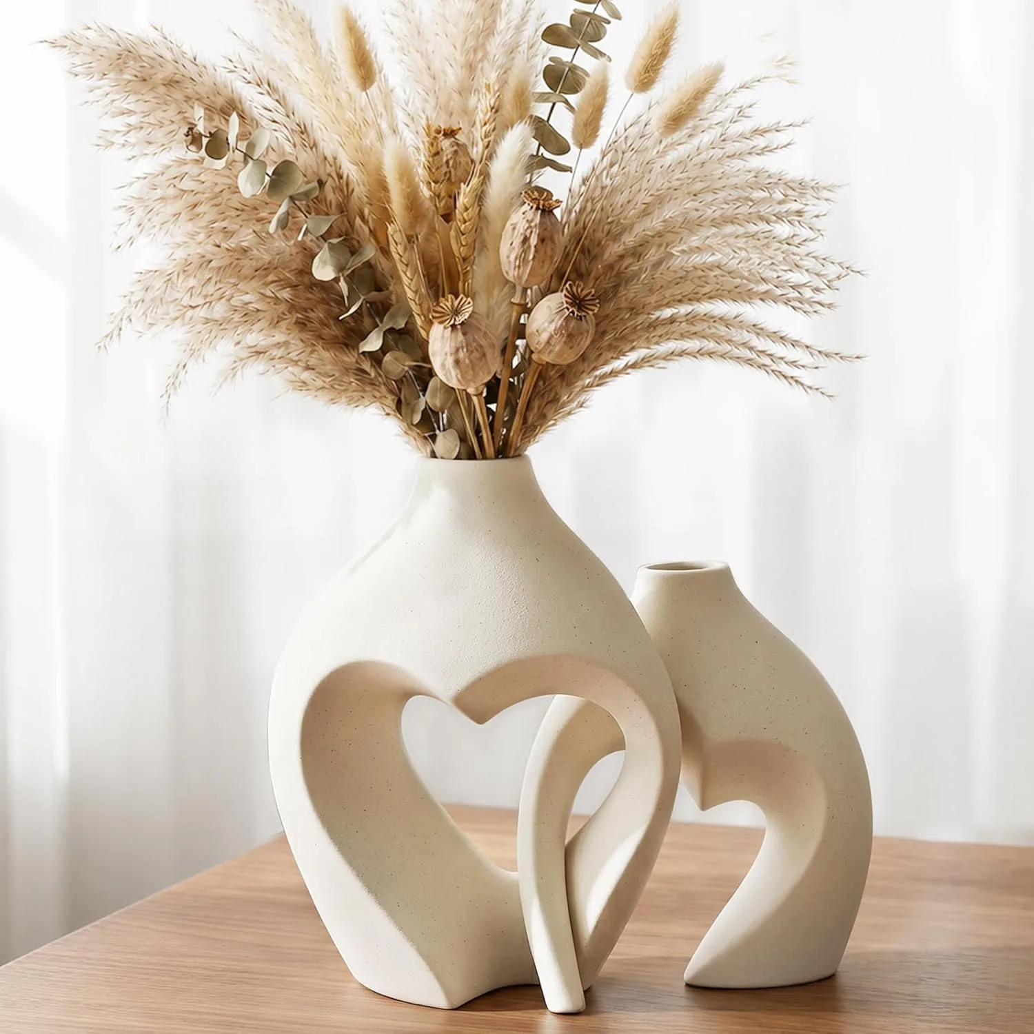 Two white ceramic heart-shaped vases styled on a wood table, showing how to incorporate romantic home accents into a neutral boho living room.