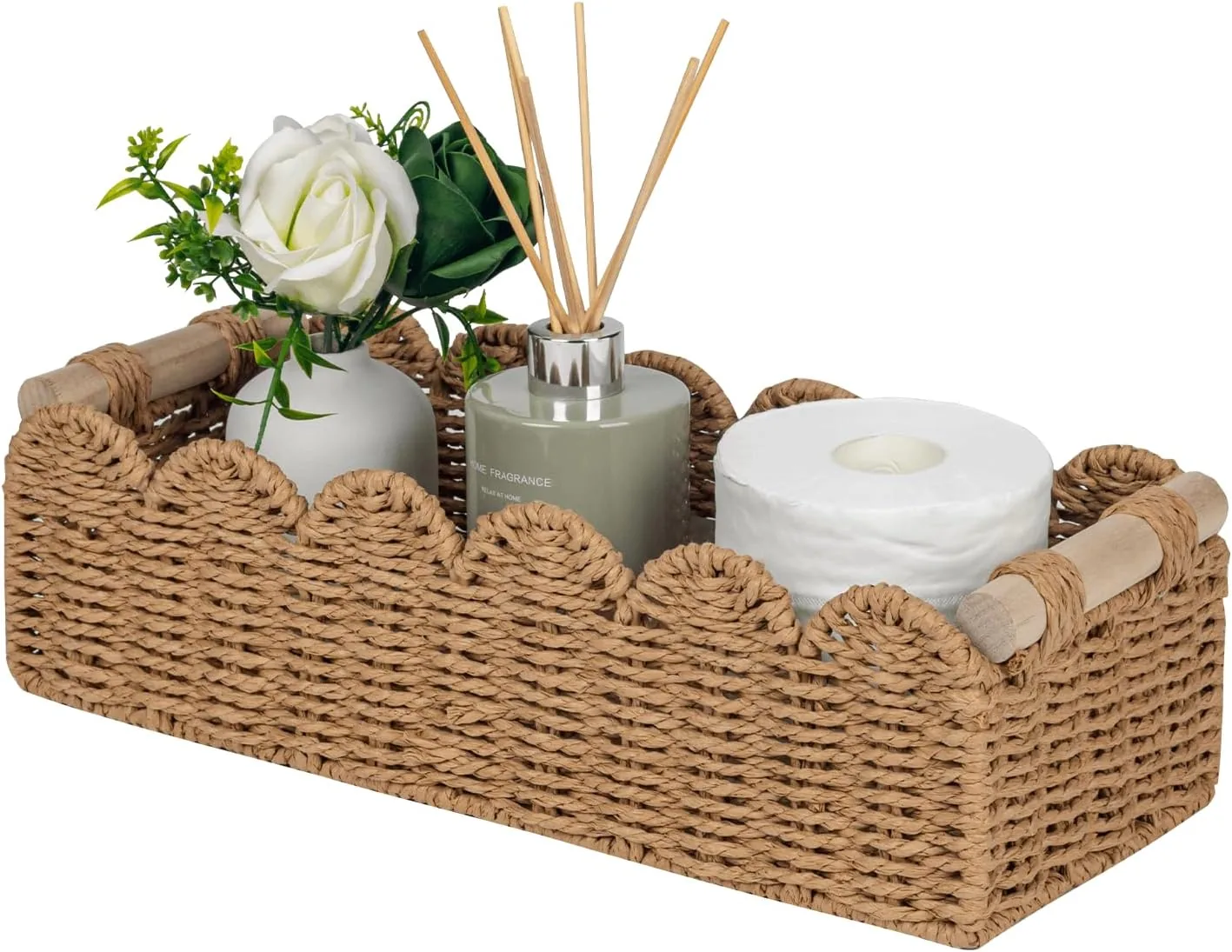 Neutral woven scalloped basket with wooden handles styled with toilet paper, reed diffuser, ceramic vase, white rose, and greenery for small bathroom basket organization.
