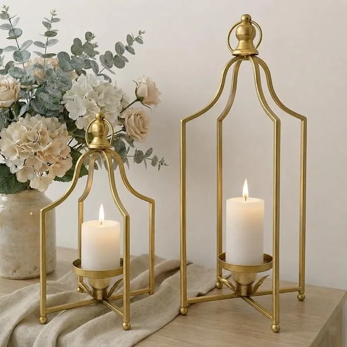Antique gold decorative lanterns with white pillar candles on a wood table styled with cream florals, eucalyptus, linen fabric, and warm neutral decor